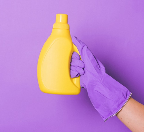 Purple gloves hand holding a yellow dishwashing liquid