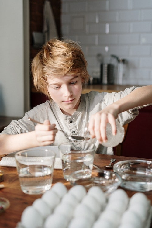 Small boy pouring clear liquid to glass jar